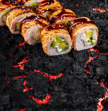 Savory sushi rolls drizzled with sauce on a fiery black and red background