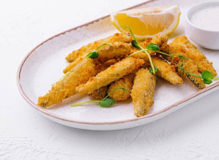 Photo for Golden fish fingers served with a side of lemon and creamy tartar sauce on a ceramic plate - Royalty Free Image