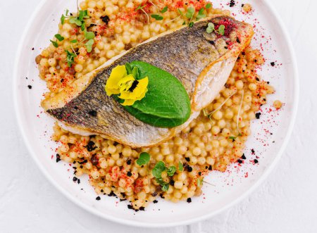 Top view of a grilled salmon fillet served with seasoned couscous, garnished with herbs