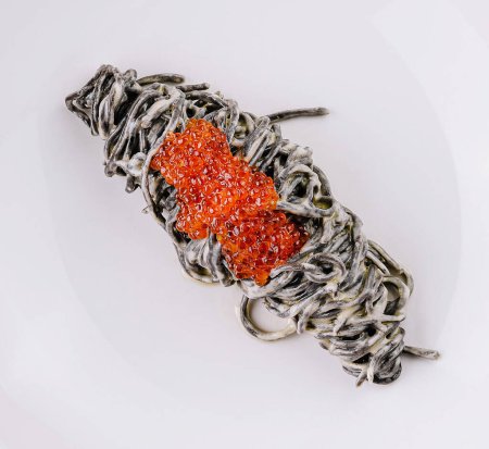 Elegant presentation of squid ink pasta topped with luxurious red caviar on a white plate