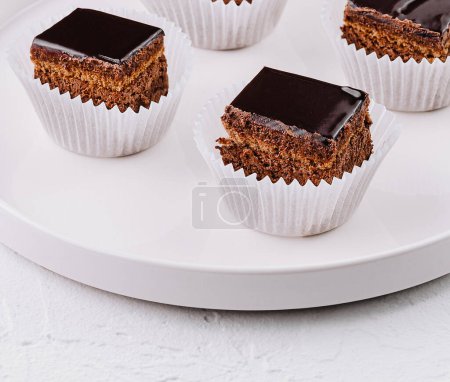 Delicious mini cakes with chocolate glaze, presented on a white plate against a textured background