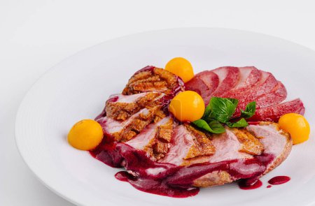 Succulent duck breast slices topped with berry sauce and fresh apricots on a white plate