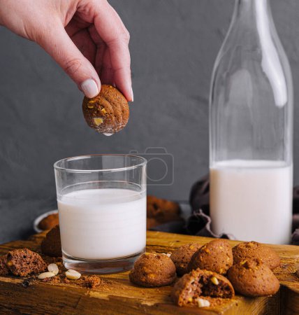 Close-up of a hand dunking a homemade cookie into a glass of fresh milk