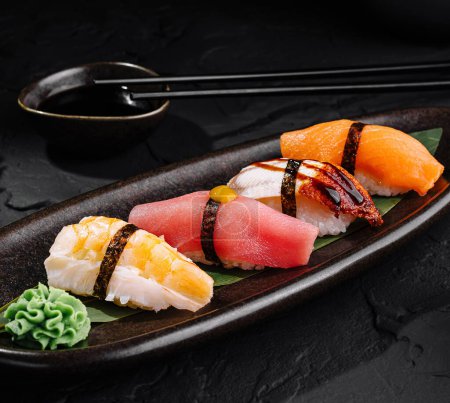 Znakomity wybór sushi nigiri serwowane na czarnej płycie z sosem sojowym i pałeczki