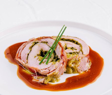 Elegante roulade de cerdo lleno de hierbas y servido con una rica salsa marrón en un plato blanco