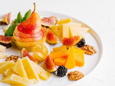 Elegant arrangement of various cheeses, fresh figs, pear, and nuts on a ceramic plate