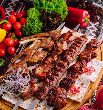 Juicy shashlik skewers served with fresh vegetables and onion rings on ethnic-patterned tablecloth