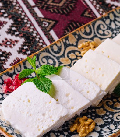 Elegant display of sliced white cheese garnished with mint leaves and walnuts on an ethnic-patterned fabric