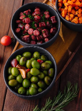 Vibrant spread of tapas including green olives, spicy sausage, and seasoned fries