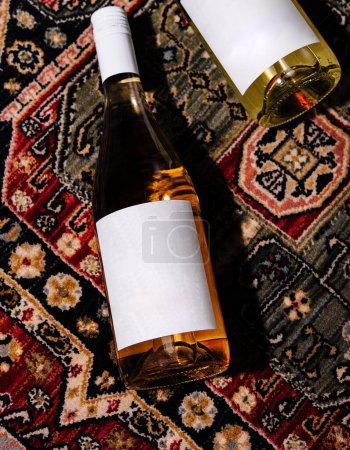 Dos botellas de vino con etiquetas modernas que descansan sobre una alfombra persa ricamente modelada
