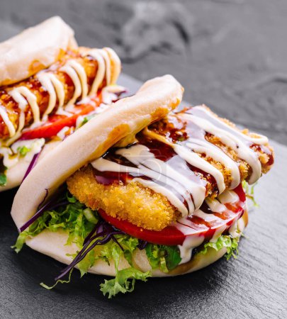 Delicious chicken burger with fresh toppings and sauces on a dark slate background