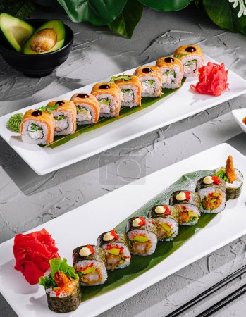 Assorted sushi rolls artfully presented on modern plates with sauces and garnish