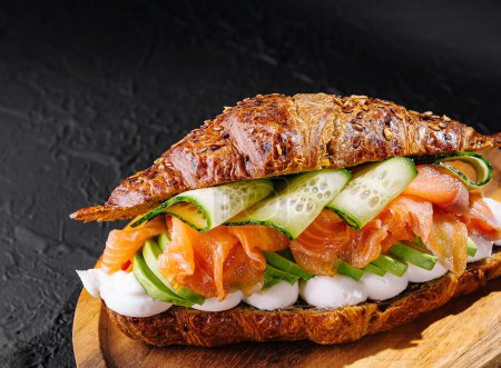 Croissant rústico de salmón ahumado gourmet con verduras frescas y queso crema en una tabla de madera