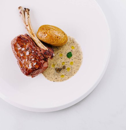 Elegant plating of a juicy lamb chop with golden roasted potatoes on a white background