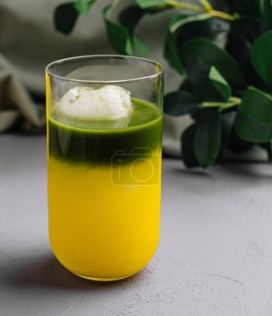Lebendiger grüner Matcha schwebt neben einem Glas frischem Mangosaft auf schickem grauen Hintergrund