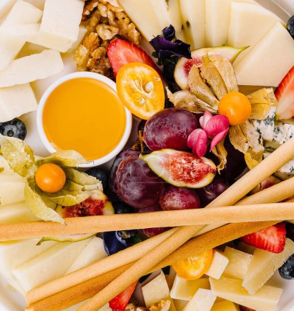 Elegante tabla de quesos con una variedad de quesos, frutas frescas, frutos secos y miel de cerca