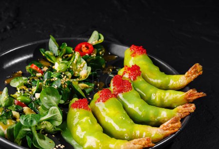 Eleganter Salat mit Avocado und Garnelen, garniert mit Sesam und Kaviar, serviert auf einem schwarzen Teller
