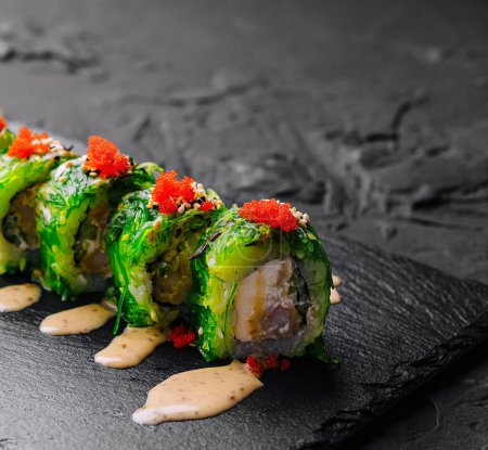 Appetizing avocado sushi roll garnished with tobiko, served on a slate board with wasabi and ginger