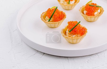 Gourmet-Mini-Törtchen mit Frischkäse gefüllt und mit Lachsrogen belegt, serviert auf einem modernen Teller