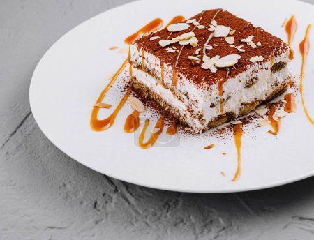 Elegant tiramisu dessert artfully plated with almond slices and caramel sauce