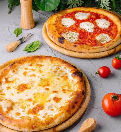 Photo for Freshly baked margherita and four cheese pizzas served on wooden boards, garnished with tomatoes and basil - Royalty Free Image