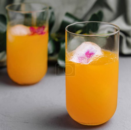 Elegantes bebidas naranjas con flores comestibles en hielo, perfectas para eventos de verano