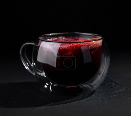 Eine moderne doppelwandige Glastasse gefüllt mit rotem Tee, isoliert vor dunklem, stimmungsvollem Hintergrund