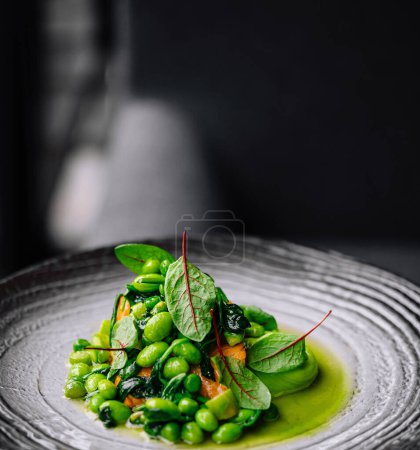 Présentation élégante d'une salade de pois verts frais avec des fleurs comestibles rouges sur une assiette décorative
