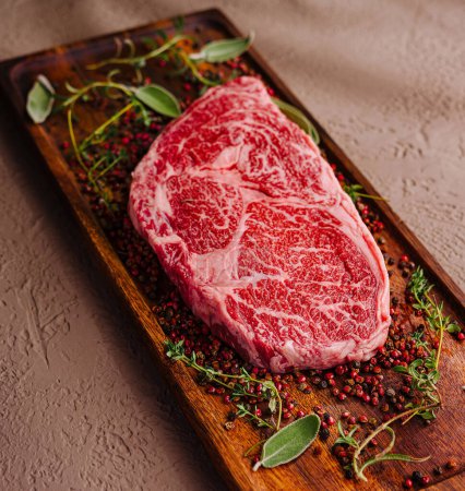 Raw, marbled ribeye steak adorned with herbs and spices, ready for cooking