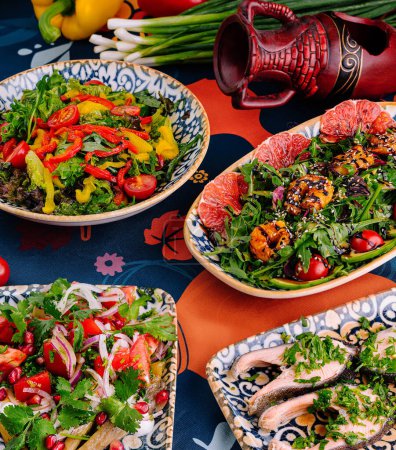 Vibrant mediterranean cuisine served in decorative bowls on a patterned tablecloth with fresh ingredients in the backdrop