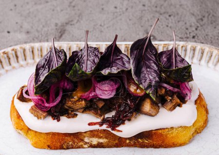 Artisanal toast topped with cream cheese, caramelized onions, and fresh purple basil on ceramic plate
