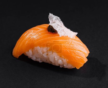 Zbliżenie smakowitego sushi z łososia nigiri ozdobionego delikatnym dodatkiem, wyizolowanego na ciemnym tle