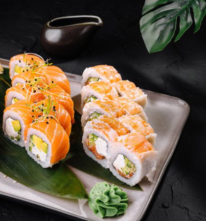 Elegante selección de sushi con rollos y sashimi sobre pizarra oscura con salsa de soja
