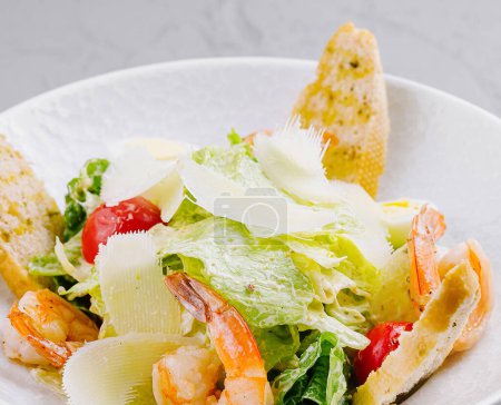 Téléchargez les photos : Salade césar appétissante avec crevettes succulentes, parmesan rasé et croûtons dorés sur une assiette blanche - en image libre de droit