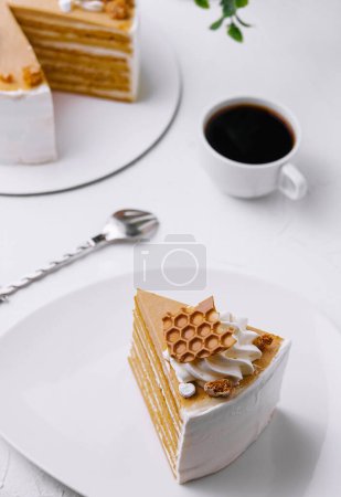 Slice of honey layer cake on a plate beside a full cake and a cup of coffee, with elegant presentation