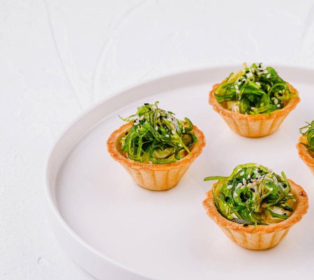 Elegant appetizer, seaweed salad in tart shells, served on a modern white plate