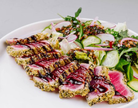 Plate of sesame-crusted tuna with fresh greens and balsamic glaze on a gray background