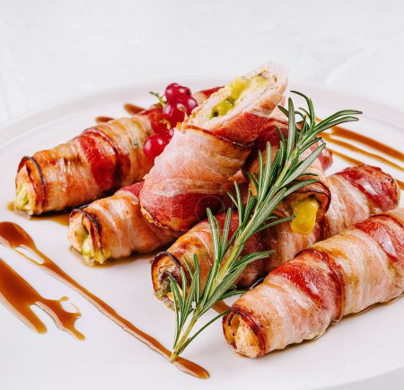 Gourmet bacon-wrapped jalapenos filled with cheese, garnished with rosemary on a white plate