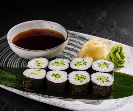 Elegancka płyta z rolkami sushi awokado, imbirem, wasabi i sosem sojowym na teksturowanej ciemnej powierzchni łupkowej