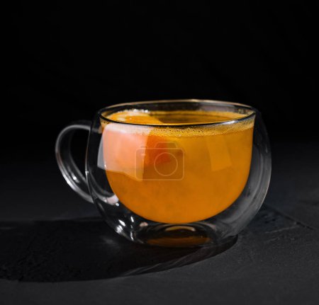 Elegant double-walled glass cup filled with hot citrus tea, highlighted against a dark background
