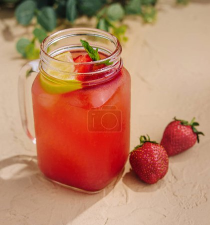 Geeiste Erdbeer-Limonade garniert mit frischer Minze und Zitrone in einem Einmachglas auf sandigem Hintergrund