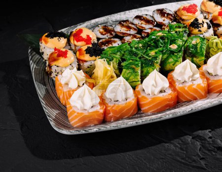 Téléchargez les photos : Sélection variée de rouleaux de sushi et de nigiri élégamment présentés sur une assiette moderne sur fond d'ardoise sombre - en image libre de droit