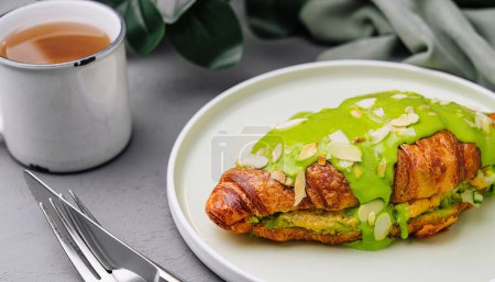 Delicious matcha croissant topped with almond flakes, served with a cup of tea