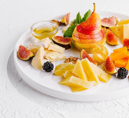 Agencement élégant de différents fromages, figues fraîches, poires et noix sur une assiette en céramique