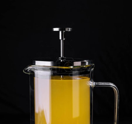 Glass french press filled with hot mint tea and lemon on a dark background