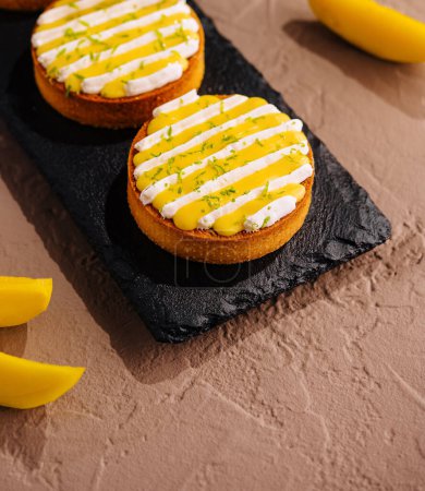 Three delicious mango tarts with creamy topping and lime zest, elegantly served on a slate board