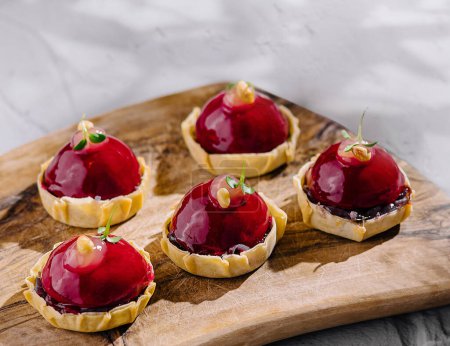 Gourmet raspberry tarts with glossy glaze on a rustic wooden serving board