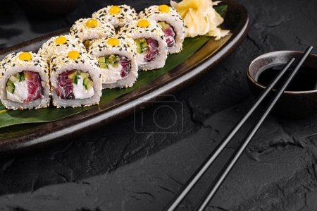 Elegancki układ sushi z pałeczkami i dzbankiem sosu sojowego na ciemnej, łupkowej powierzchni