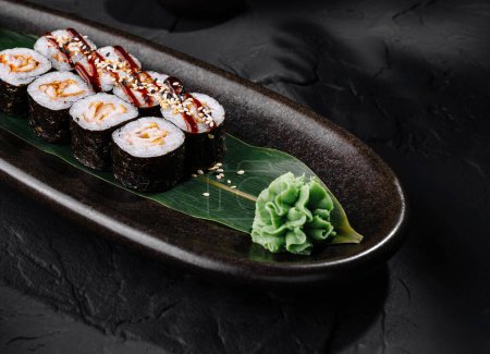 Artfully presented sushi rolls on a leaf, with wasabi, ginger, and soy sauce on a stylish slate plate
