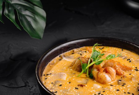 Délicieux curry de crevettes garni d'herbes dans un bol à côté du riz, sur un fond texturé foncé